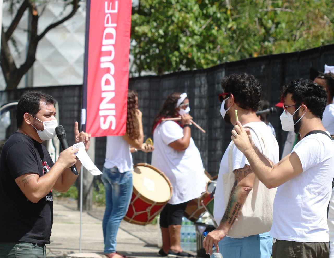 #PraCegoVer Fotografia em frente ao Fórum Rodolfo Aureliano, no Recife, reúne parte da diretoria do SINDJUD-PE com grupo de maracatu ao fundo durante mobilização para a Assembleia Geral do dia 31/01.