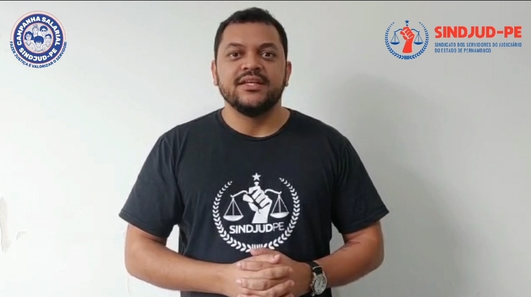 #PraCegoVer Imagem do Coordenador-Geral do SINDJUD-PE, Alcides Campelo, em ambiente interno. Campelo está posicionado em frente a uma parede branca e veste camisa preta com a logomarca do Sindicato.
